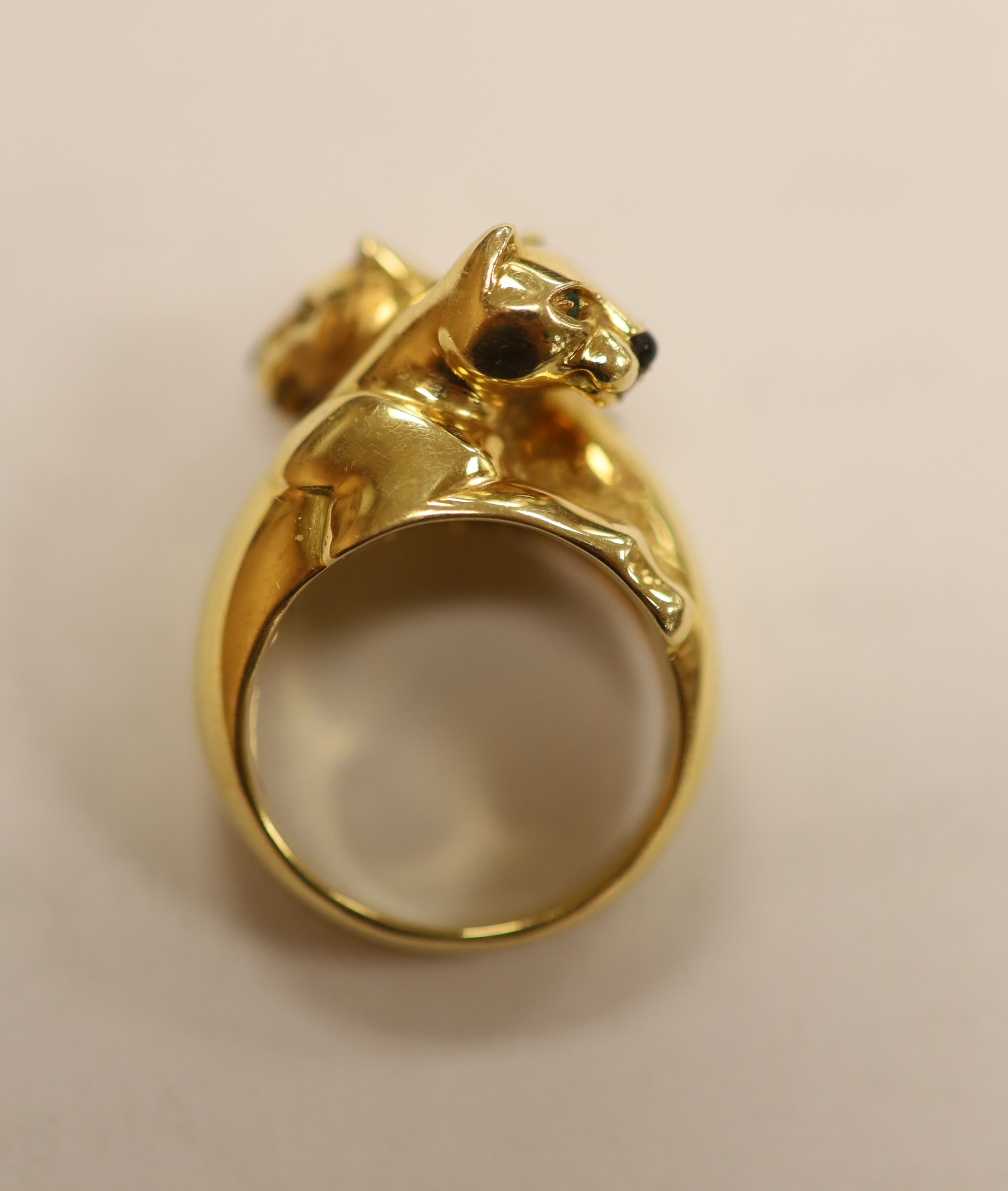 An early 1990's Cartier 18ct gold, black onyx and emerald set twin leopard's head crossover ring